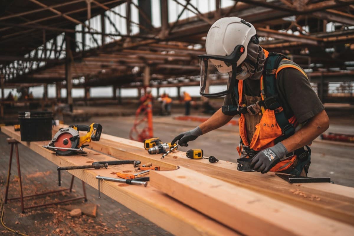 A worker in a hard hat and safety vest drilling into a beam